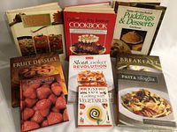 Nine cookbooks arranged standing and flat, shows titles and cover images with food photography