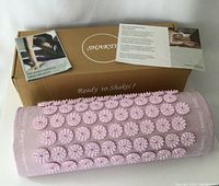 Pink Shakti acupressure pillow on a surface next to brown box and informational pamphlets.