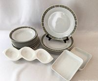 View of porcelain bowls, plates with gold and black geometric trim, divided serving dish and two small white porcelain rectangular dishes.