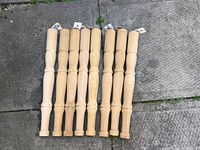 Photo showing eight wooden table legs laid out on pavement, displaying turned design and natural wood finish.