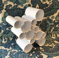 Cluster of white tubular circular compartments of the Umbra Cru wine rack against a paisley patterned fabric background.