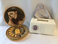 Philips Beauty Set round case open showing multiple yellow attachments inside, case cover with vintage photo, fabric bonnet accessory seen