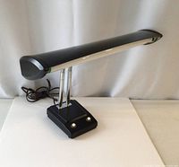 Side view of the vintage black desk lamp showing the elongated light cover and dual chrome arms connected to the base with two control knobs.