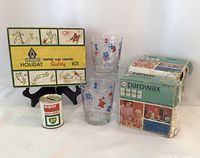 Overview photo showing the lot contents including the United Gas Holiday Safety Kit box on display stand, the BP tin bank, the two Esso flag glasses, and the Esso Parawax wax boxes stacked.