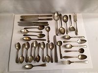 Full set of vintage silverplate cutlery laid out on a white surface including various spoons, forks, and knives.