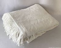 Folded white chenille bedspread showing fringe edge and texture.