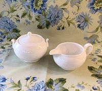 Wedgewood cream pitcher and sugar bowl with lid on a floral cloth background