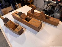 Three antique wooden hand planes displayed on a white surface showing front and side views.
