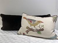 Photo showing the two cushions, one is a long chocolate brown faux fur covered pillow and the other is a bird patterned pillow with natural fabric and grey piping.