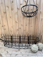 Top-down view of rectangular metal planter and round hanging planter placed on wooden floor with two decorative concrete balls nearby.