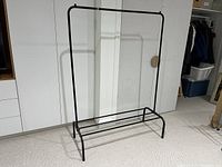Fully assembled black metal hanging rack shown empty on carpeted floor against white wall.