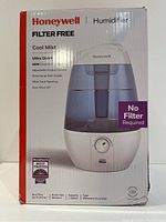 Front view of the Honeywell humidifier box showing product name, main features including filter-free operation, cool mist output, ultra quiet function, adjustable output control, wide tank opening, and auto shut off. The box also shows 1 year warranty.