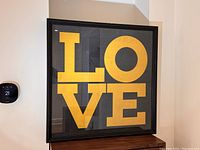 Front view of the framed LOVE print on a wall showing the bold yellow letters on black background.
