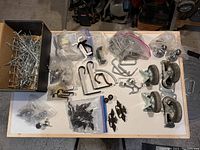 Full top-down view of all hardware items including bagged hooks, assorted handles and pulls, and castors on table.