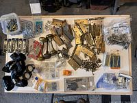 Overall top-down view of all hardware items laid out on table including hinges, knobs, screws, plumbing parts, and packages.
