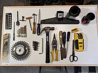 Photo showing a collection of miscellaneous hand tools, power tool accessories, drill bits, vacuum nozzles and stud sensor laid out on a white surface for clarity.