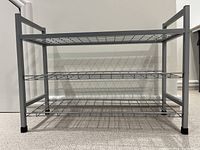 Front view of a three-tier metal shoe rack with wire mesh shelves and sturdy rectangular frame.