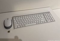 Wireless keyboard, white wireless mouse, and USB dongle shown from a top-down angle on a table.