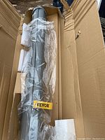 Packed retractable side awning unit in open cardboard box showing gray metal cassette housing with VEVOR label and foam padding