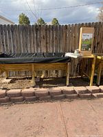 Two VegTrug raised garden beds with black liners alongside boxed and loose accessories against fence