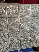 Six square metal nail-up wall tiles stacked with visible embossed repeated circular design pattern and artisan silver washed white finish.