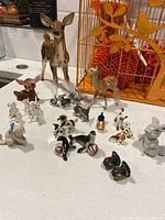 Photo showing multiple animal figurines including deer, dogs, cats, seals, and birds with a decorative orange background.