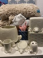 Photo showing the ceramic turtle themed bathroom set with planter, Kleenex holder, toothbrush holder cup, and soap dish, along with the pink Fossil-Free dinosaur toothbrush holder and folded white towels in the background.