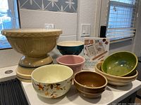 Group photo showing all bowls in various sizes, colors, including a large beige pedestal bowl, blue, pink, green, brown nested, and floral patterned bowls