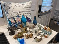Overview of the bird figurines and decorative pillow arranged on a counter. Shows multiple bird figurines in wood, ceramic, and metal along with a pillow featuring bird artwork and French handwriting.