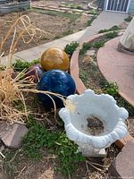 Photo showing the large white cement planter and three colored ceramic spheres arranged on garden soil near edging.