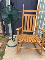 Photo showing a wooden rocking chair and a Holmes standing fan placed outdoors.