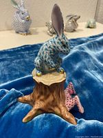 Front view of teal fishnet rabbit atop tree stump showing overall design and color