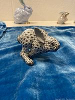 Front right side view of porcelain rabbit figurine on blue cloth, showing fishnet pattern and glossy finish
