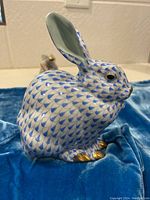 Side view of the rabbit figurine on a blue cloth background showing fishnet pattern and gold accents