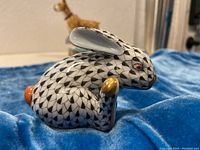 Side view of Herend hand-painted bunny figurine with black fishnet pattern, gold accent on paw, orange foot, and red eye.
