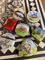 Seven Limoges porcelain boxes featuring various '12 Days of Christmas' illustrations, including birds and holiday symbols, all with brass hinges and clasps.