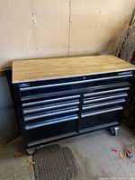 Front view of black Husky tool chest with wood top on caster wheels