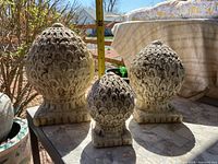 Photo showing three ceramic decorative finials of varied sizes placed outdoors on a tile surface, measuring tape in background for scale.