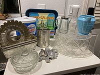 Wide view of vintage kitchen items showing aluminum baking pans, glass covered bowl, glass syrup pitcher, blue ceramic pitcher, metal tray, and other items.