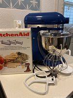 Front view of royal blue Artisan mixer with stainless bowl, attachments and boxed pasta set