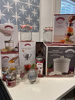 Kilner brand new kitchen glass jars and storage set in original packaging, displayed on countertop with various jar types and boxes visible.