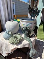 Table with soapstone frogs, large apple and pear sculptures, floral planter, wrought iron mermaid, and bell