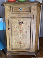 Front view of the painted corner cabinet showing drawer and door with floral design.