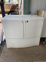 Front view of white plastic outdoor storage unit showing woven rattan style doors and drawer with lock latch.
