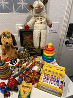 Overview of toys on table including plush toys, wooden stacking rings, ladybug figurines, Crayola crayons box, See and Spell toy, and framed Spider-Man picture