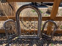 Set of three weathered wooden and metal framed plant holders with arched tops, placed outside on gravel under a covered patio.