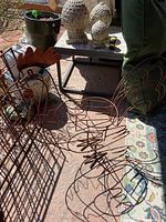 Wrought iron rooster plant stand and trellises on patio with garden items in background