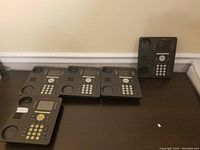 Five Avaya 9611G phones arranged on a dark desk surface, missing handsets and cables, showing overall used condition.