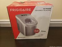 Frigidaire ice maker box showing image of the silver ice making machine, capacity 26 lbs 12 kgs, box exhibits wear and some damage.