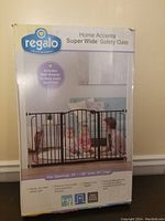 Front of box showing product image of the black metal Regalo Home Accents Super Wide Safety Gate with specifications and features listed.